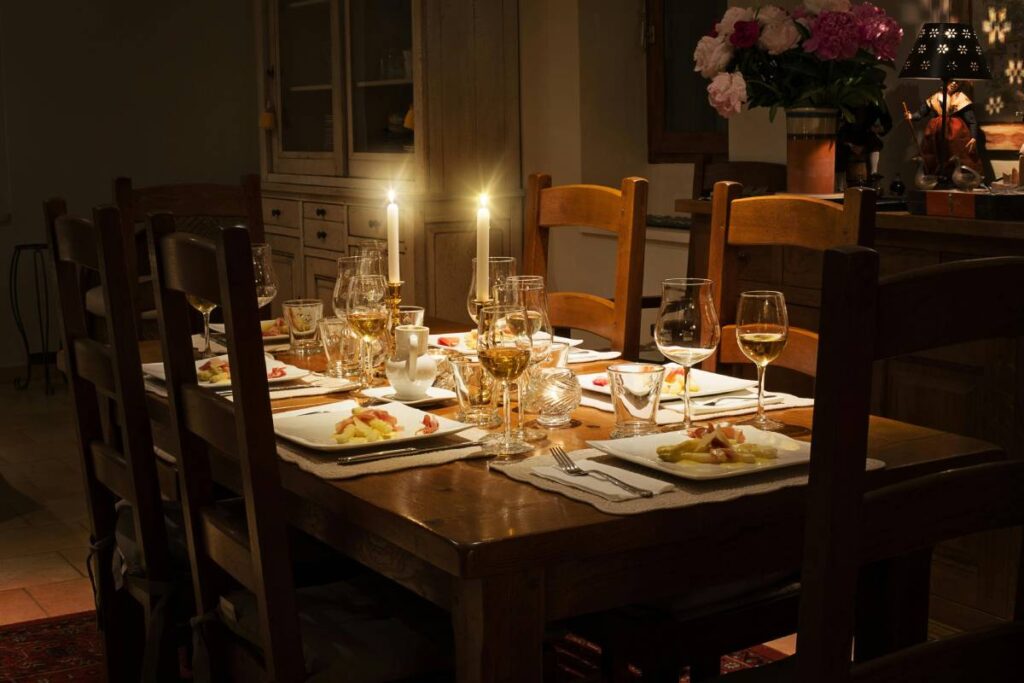 Tavola elegante apparecchiata secondo il galateo, con calici di vino, piatti bianchi e candele accese per una cena raffinata.
