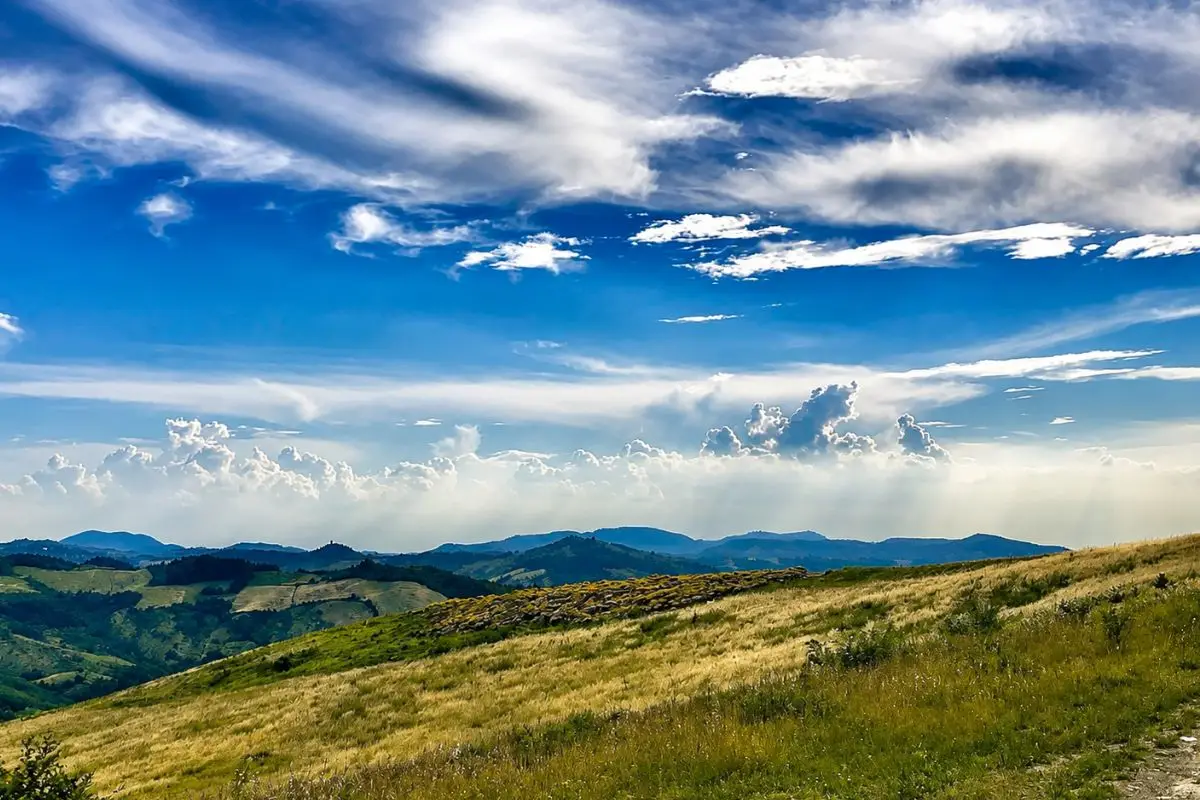 Panorama delle colline dell’Oltrepò Pavese con prati, rilievi appenninici e cielo attraversato da grandi nuvole.